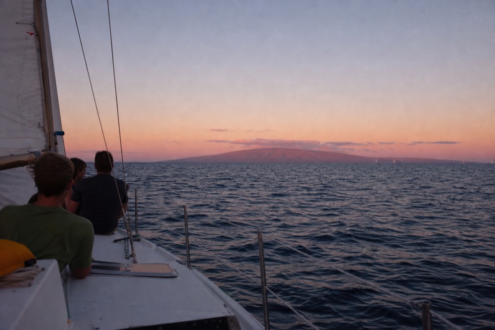 View from a boat deck with an unobstructed sea horizon in every direction, one distant island profile catching the last direct light