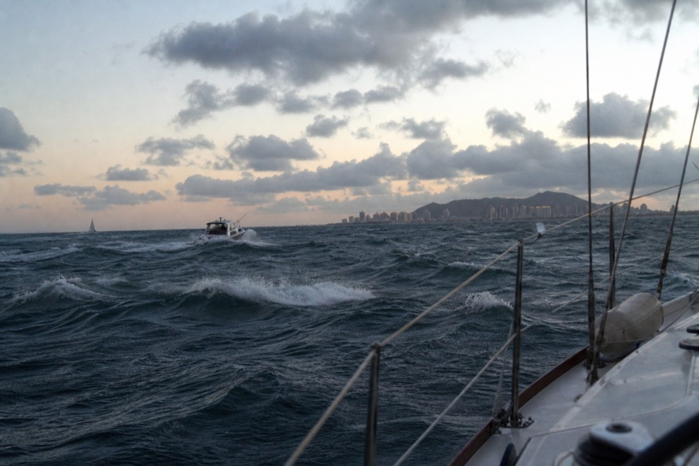 Whitecaps and wind-driven chop across a bay mouth in strong afternoon light, a small boat pitching in the middle distance