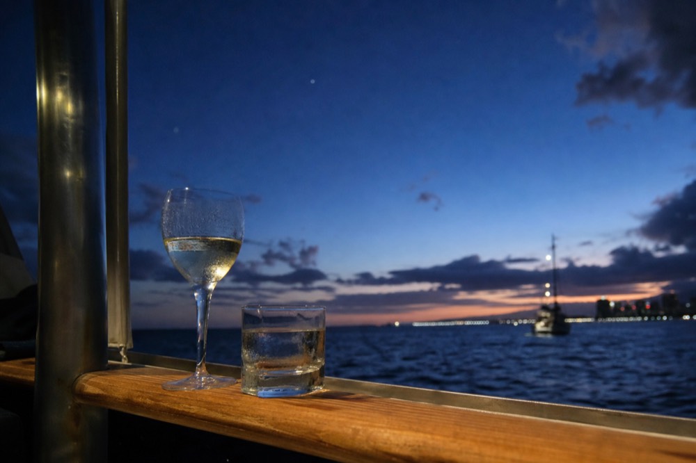 Two glasses left on a boat's teak rail against a deep blue post-sunset sky with the first stars showing