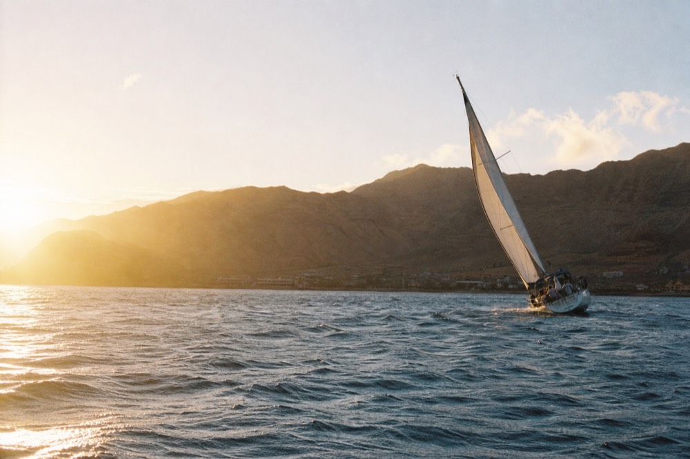 Whitecaps and wind streaks across a bay with a dry mountain saddle behind and a sailing boat heeling in the chop