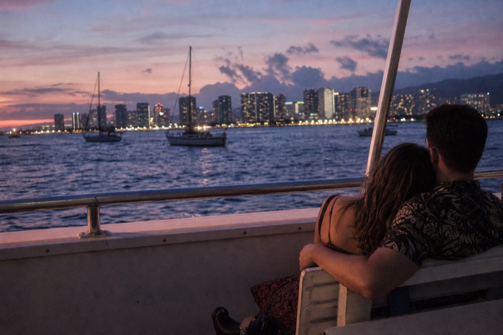Almost empty boat deck at blue hour with a couple seated close on a bench and shoreline lights behind them