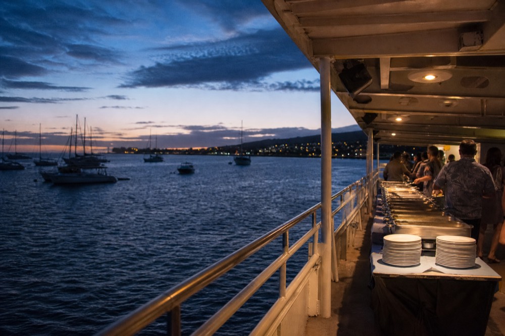 Buffet line set out along a wide covered deck with plates and warming trays and guests helping themselves