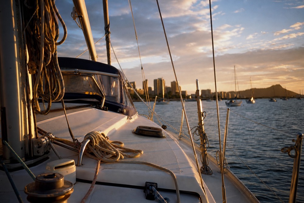 Warm low sunlight raking across a boat's white deck and coiled lines about forty minutes before the sun reaches the water