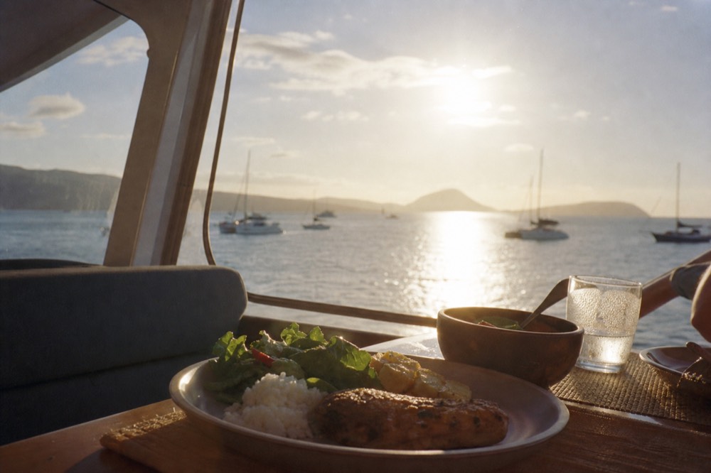 Plated dinner on a boat table with the sun still well above the horizon through the window behind it