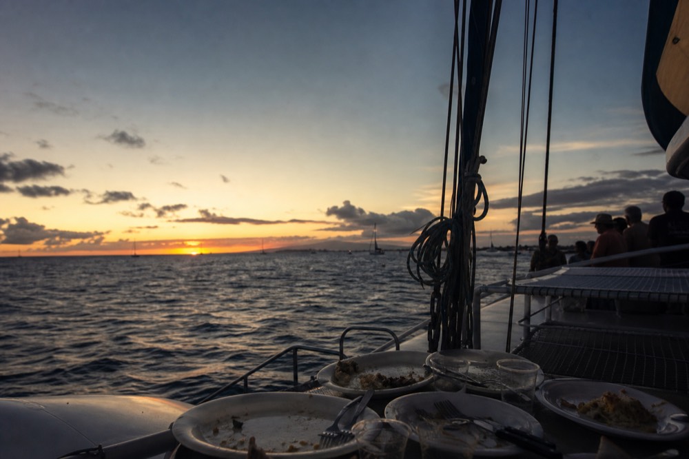 Deck of a catamaran at blue hour with empty dinner plates on a table and the last band of color low over the water