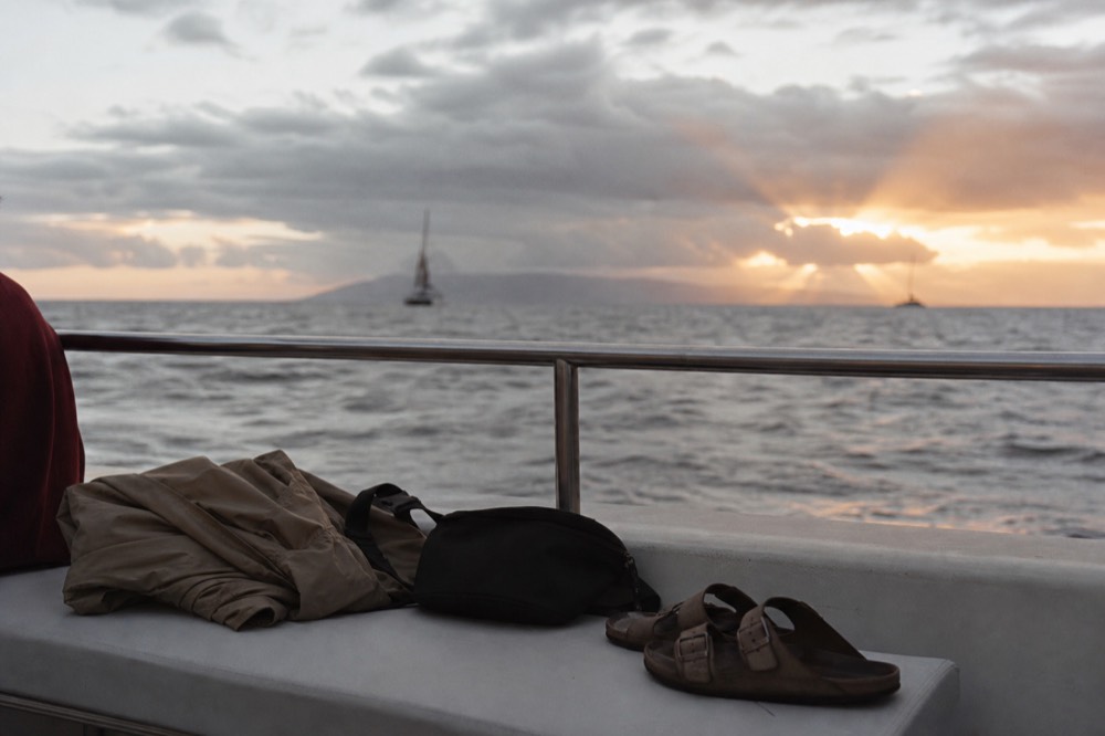A light jacket, sandals and a small closed bag laid on a boat bench with the darkening sea beyond the rail