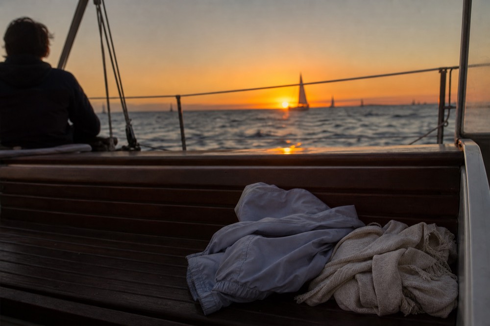 Folded lightweight jacket and a soft wrap resting on a boat bench with warm low light falling across them