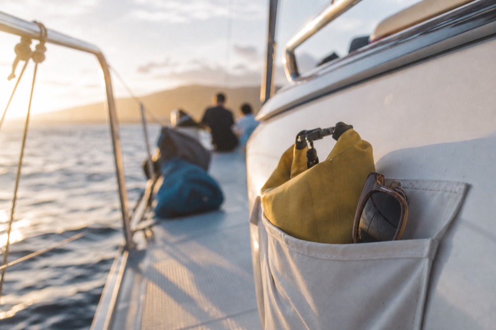 Small dry bag and a pair of sunglasses tucked into a boat's side pocket with the ocean out of focus beyond