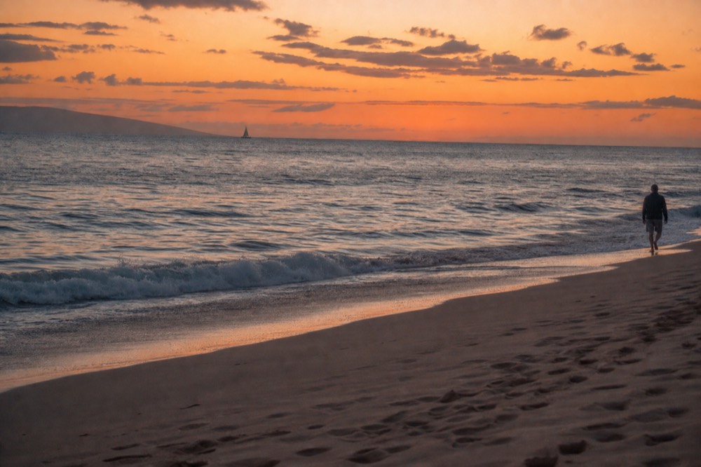 Beach at civil twilight twenty minutes after the sun has gone with the sky still orange the water pale grey and one figure walking the waterline